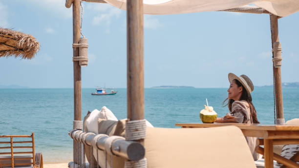 a beautiful young asian woman holding and drinking coconut juice on the beach