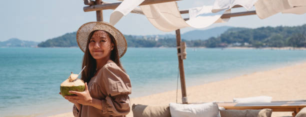 a beautiful young asian woman holding and drinking coconut juice on the beach