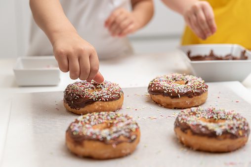 Children decorating doughnuts with colorful splashes in the kitchen at home