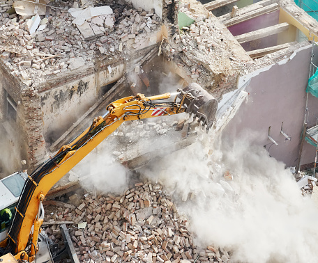 Old brick building demolition with an excavator bucket in dust cloud, view from above.