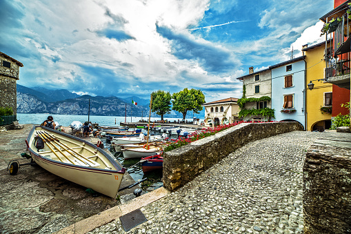 Unique view of a italian village on Garda lake with colored houses, boats at harbor and a pedestrian brick bridge against a cloudy and blue sky, Verona, Italy