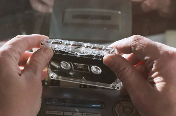 Audiocassette in men's hands on the background of a tape recorder with the widely used symbols without a trademark
