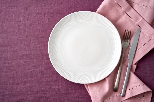 istock Clean empty white plate, fork and knife on bright blueberry red linen tablecloth on table, mockup 1303990513