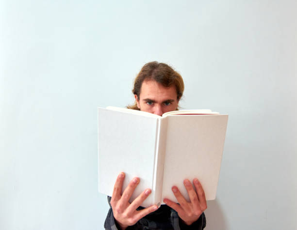 A Caucasian man reading a white book on the background of white wall