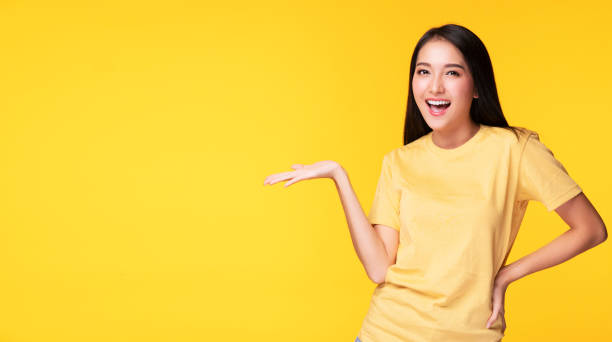 istock Cheerful young woman holding her hand with product or empty copy space while standing over isolated on yellow background 1303992985