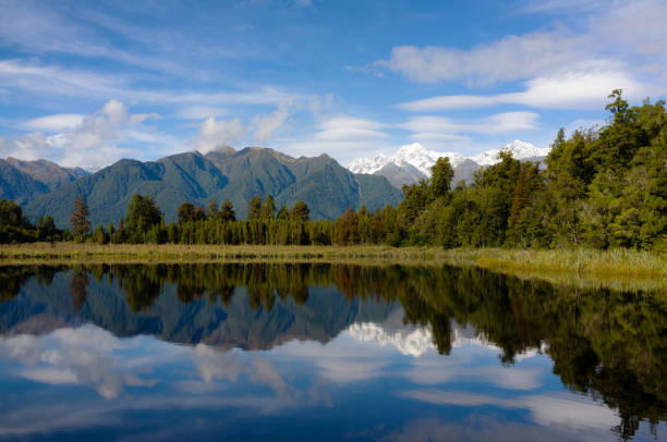 Lake Matheson, On New Zealand's South Island Spectacular Lake Matheson on New Zealand's South Island. In the distance, lenticular clouds drift across the snowcapped peaks of Mt Cook and Mt Sefton. mirror lake stock pictures, royalty-free photos & images