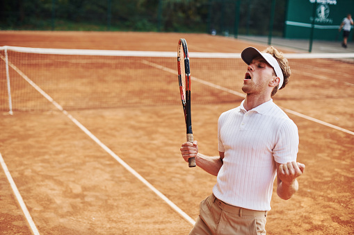 Celebrating victory. Young tennis player in sportive clothes is on the court outdoors.