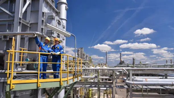 Photo of teamwork: group of industrial workers in a refinery - oil processing equipment and machinery