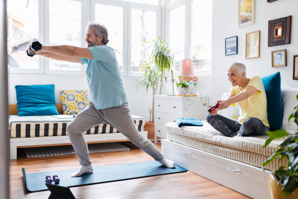 istock Senior man doing exercises while senior woman playing video games on couch 1303998037