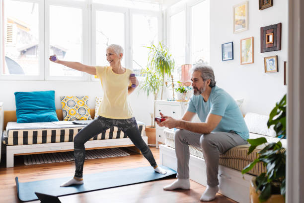 Senior woman doing exercises while senior man playing video games on couch