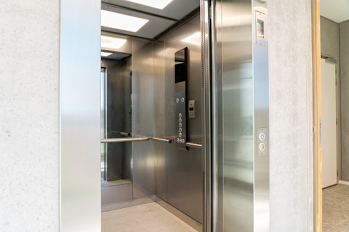 An emply elevator with its doors open in a modern office building.