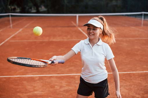 Young female tennis player in sportive clothes is on the court outdoors.