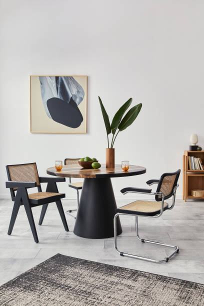 istock Stylish composition of dining room interior with design table, modern chairs, decoration, tropical leaf in vase, fruits, bookcase, abstract mock up paintings and elegant accessories in home decor. 1303999497