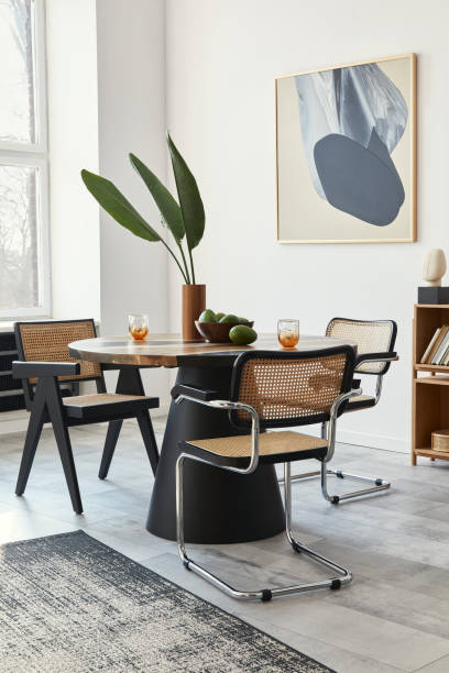 istock Stylish composition of dining room interior with design table, modern chairs, decoration, tropical leaf in vase, fruits, bookcase, abstract mock up paintings and elegant accessories in home decor. 1303999551