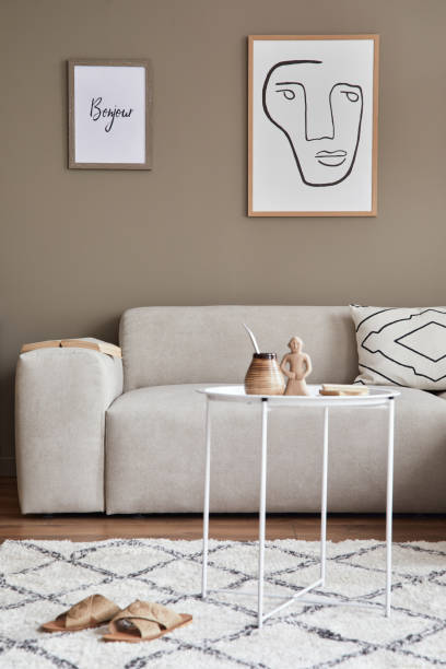 istock Modern composition in stylish living room interior with design neutral sofa, coffee table, mock up poster frames, carpet, decoration and elegant personal accessories in home decor. Template. 1304000269