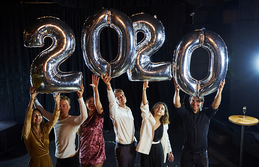 Cheerful group of people with drinks and balloons in hands celebrating new 2020 year.
