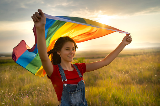 LGBT girl holding a rainbow flag against the wind and smiling