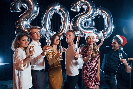 Cheerful group of people with drinks and balloons in hands celebrating new 2020 year.