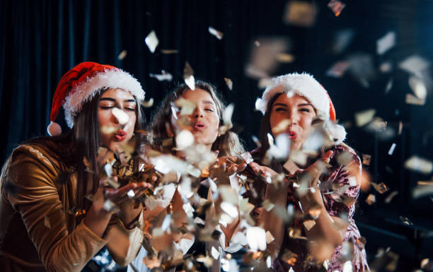 Three positive girls blowing gold colored confetti from their hands.