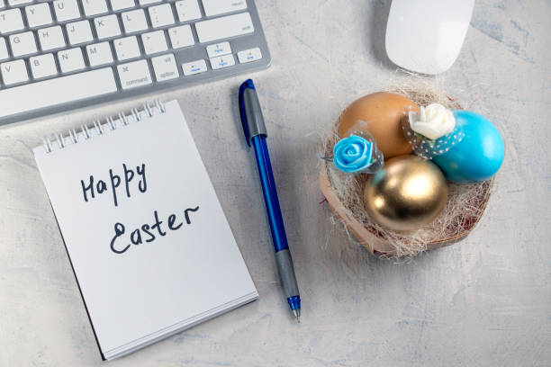 Words Happy Easter in a notebook on the desktop with colored eggs in the nest. Easter in office stock photo