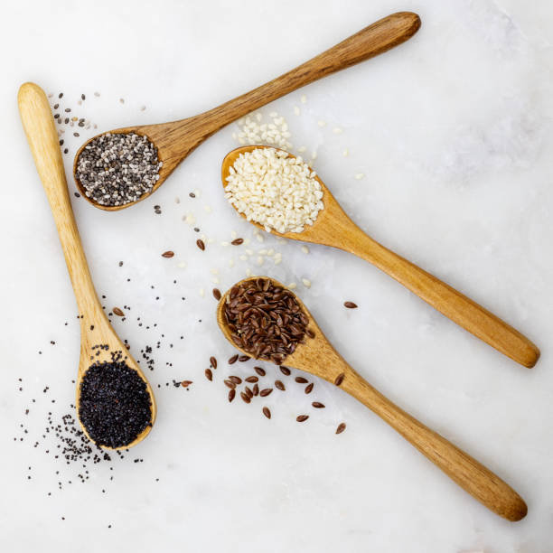 Different edible seeds in wooden spoons on marble top Chia seeds, linen seeds, sunflower seeds, sesame seeds poppy seed stock pictures, royalty-free photos & images
