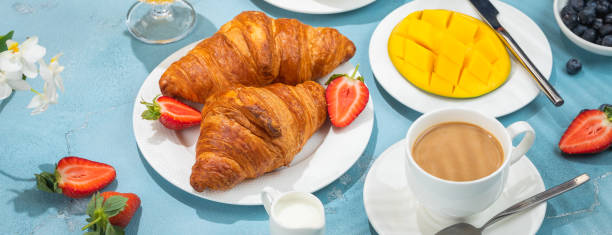 istock Luxury sunny continental breakfast on blue concrete background table with tropical plants shadows, banner 1304009407