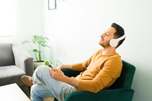 Relaxed adult man enjoying his favorite song and listening to music with headphones. Young man smiling with his eyes closed and sitting in the living room