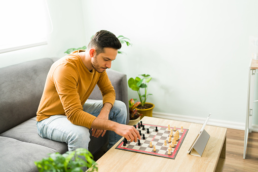 Handsome man playing chess online with a second player with his tablet. Hispanic man sitting on the sofa and enjoying a board game