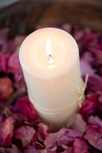A burning candle in a bed of pink flowers