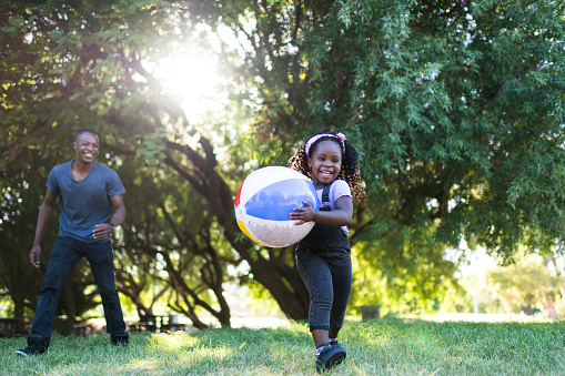 Smiling young girl playing with a beach ball in the park with her father