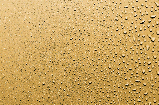 Close up of water drops on smooth surface, gold background