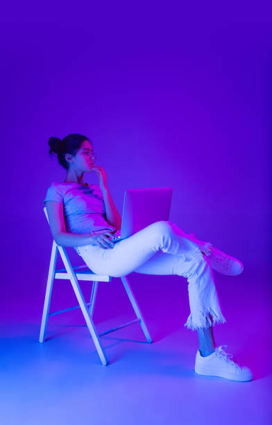Beautiful girl using laptop isolated on multicolored background in neon light.