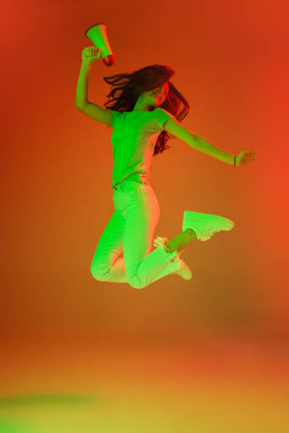 istock Young female model with megaphone jumping on neon light background. 1304021661