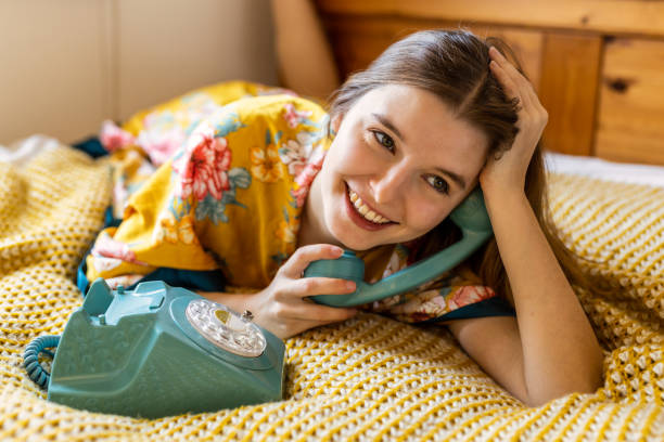 Happy blond young woman in bed late in the morning, talking on the phone with a friend stock photo