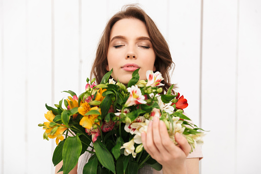 Young cheerful florist woman standing with flowers in workshop. Eyes closed.