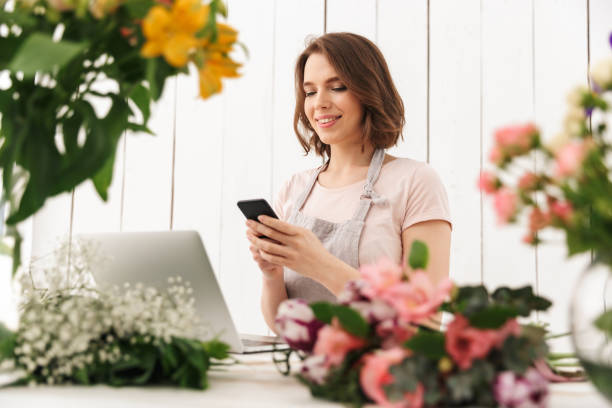 istock Cute cheerful florist lady using laptop computer chatting by mobile phone. 1304025627