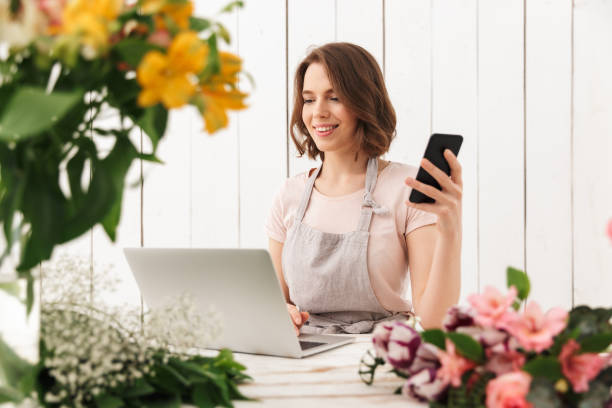 istock Cute cheerful florist lady using laptop computer chatting by mobile phone. 1304026393