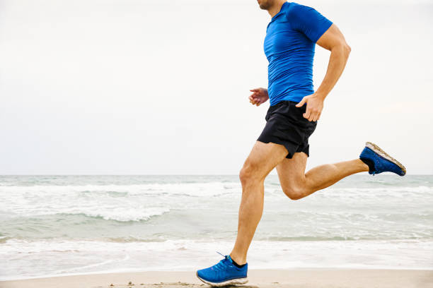 closeup male runner running sandy beach closeup male runner running sandy beach in background of sea and sky running shorts stock pictures, royalty-free photos & images
