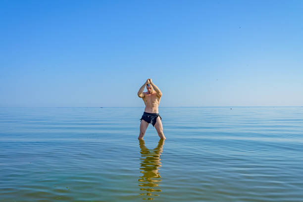 A man in a loincloth standing in water with a knife in his hand.