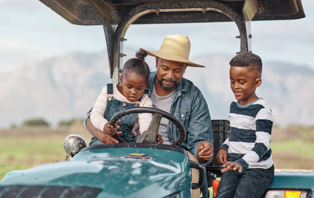 Driver's ed looks a bit different living on a farm Shot of a mature man driving a tractor with his adorable son and daughter on a farm african father stock pictures, royalty-free photos & images