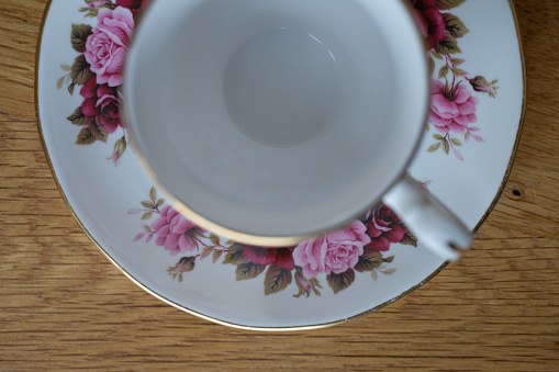 Close-up of a single empty bone China footed tea cup and saucer with a flower pattern, made in England, from directly above standing on a wooden table