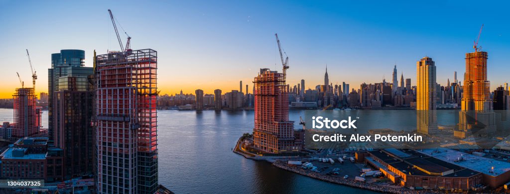 New luxury residential towers' construction on the waterfront of East River in Greenpoint, Brooklyn, and Hunters Point, Queens, around Newtown Creek, with the scenic view of Manhattan skyline. Extra-large high-resolution aerial panorama. New residential towers' construction on the waterfront in Brooklyn and Queens, with the scenic view of Manhattan skyline, at sunset. Construction Site Stock Photo