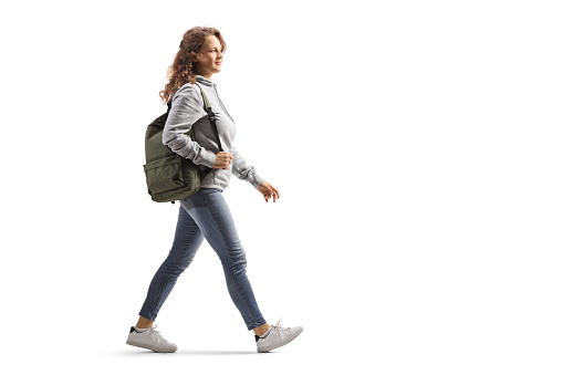 Full length profile shot of a female student in jeans with a backpack walking