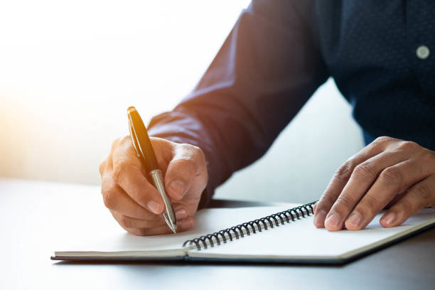 istock Close-up of man hand using writing pen memo on notebook paper or letter, diary on table desk office. Workplace for student, writer with copy space. business working and learning education concept. 1304039861