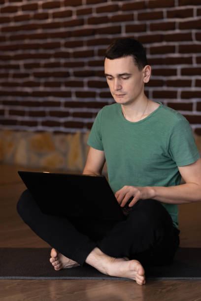 istock Student sitting on floor of his apartment with laptop and notes studying 1304040870