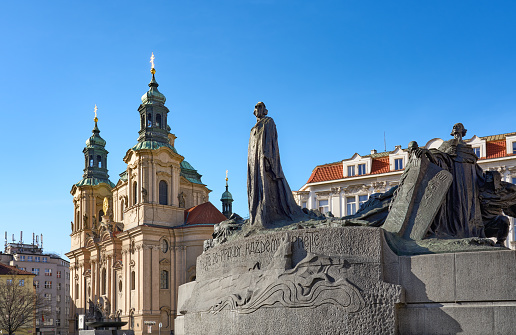 Prague, Czech Republic - March 2, 2020 The Jan Hus Memorial is designed by Ladislav Šaloun and unveiled in 1915. St. Nicholas' Church in the background