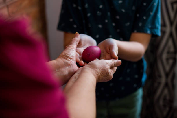 Young boy taking Easter egg that his granny is giving him. Selective focus. Grandson is taking purple Easter egg that his granny is giving him. They are standing in living room, enjoying in Easter. orthodox church easter stock pictures, royalty-free photos & images