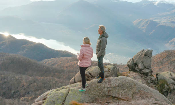 istock Couple stand on cliff edge above lake and mountains 1304045054