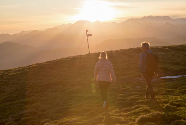 istock Couple walk up high grassy field, trail marker 1304045276