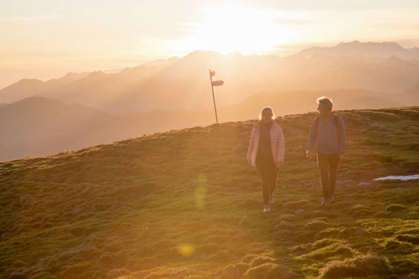 istock Couple walk up high grassy field, trail marker 1304045376